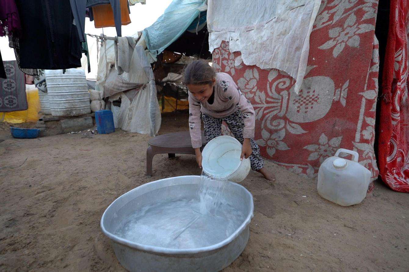 A girl pours water into a tub in front of a tent in Gaza.