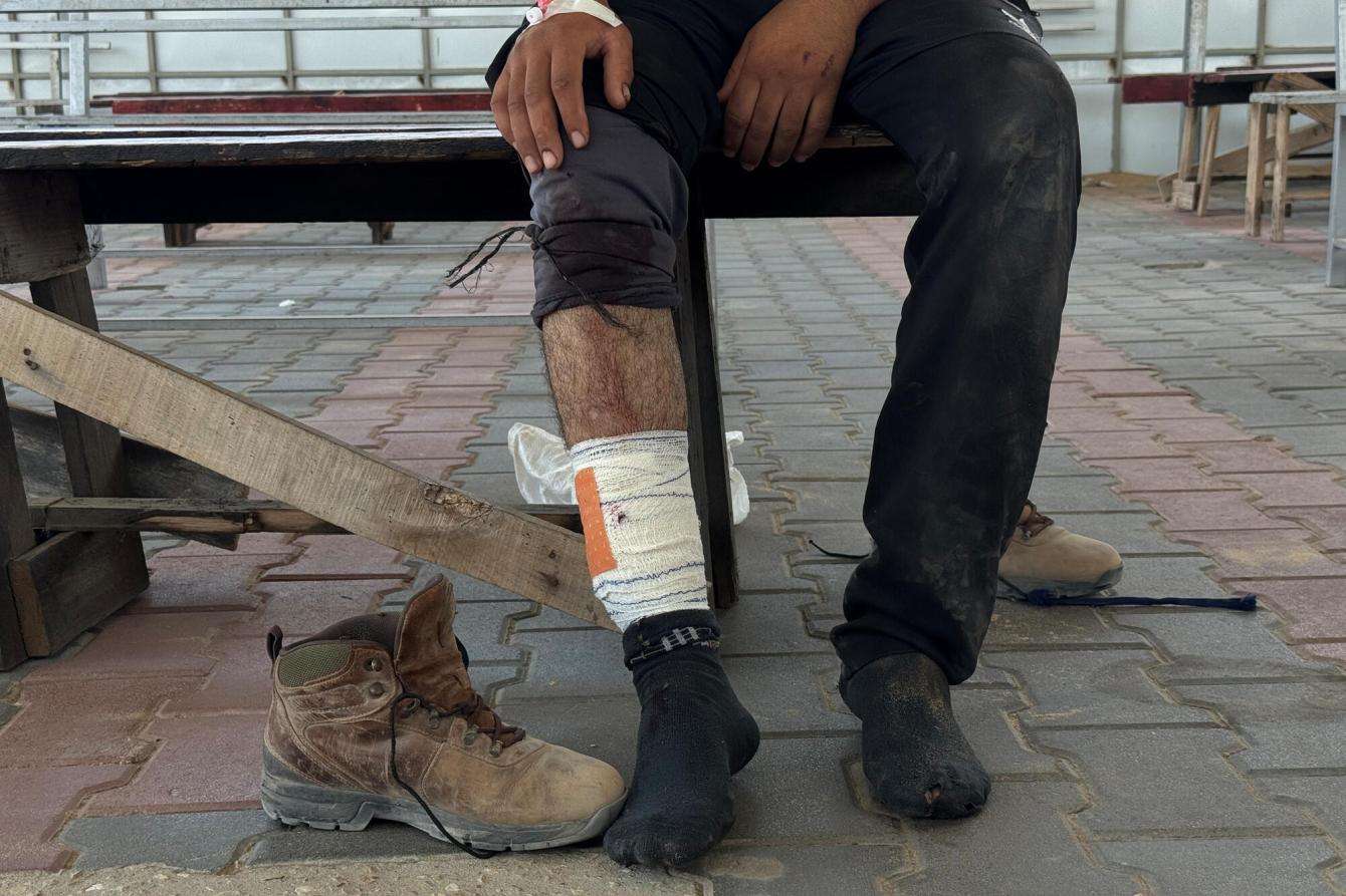 A man with a bandaged leg sits on a bench in Gaza, Palestine.
