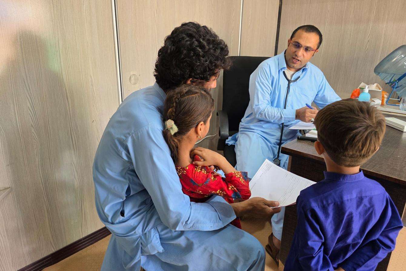 A doctor examines a young girl sitting on her father's lap in Pakistan.